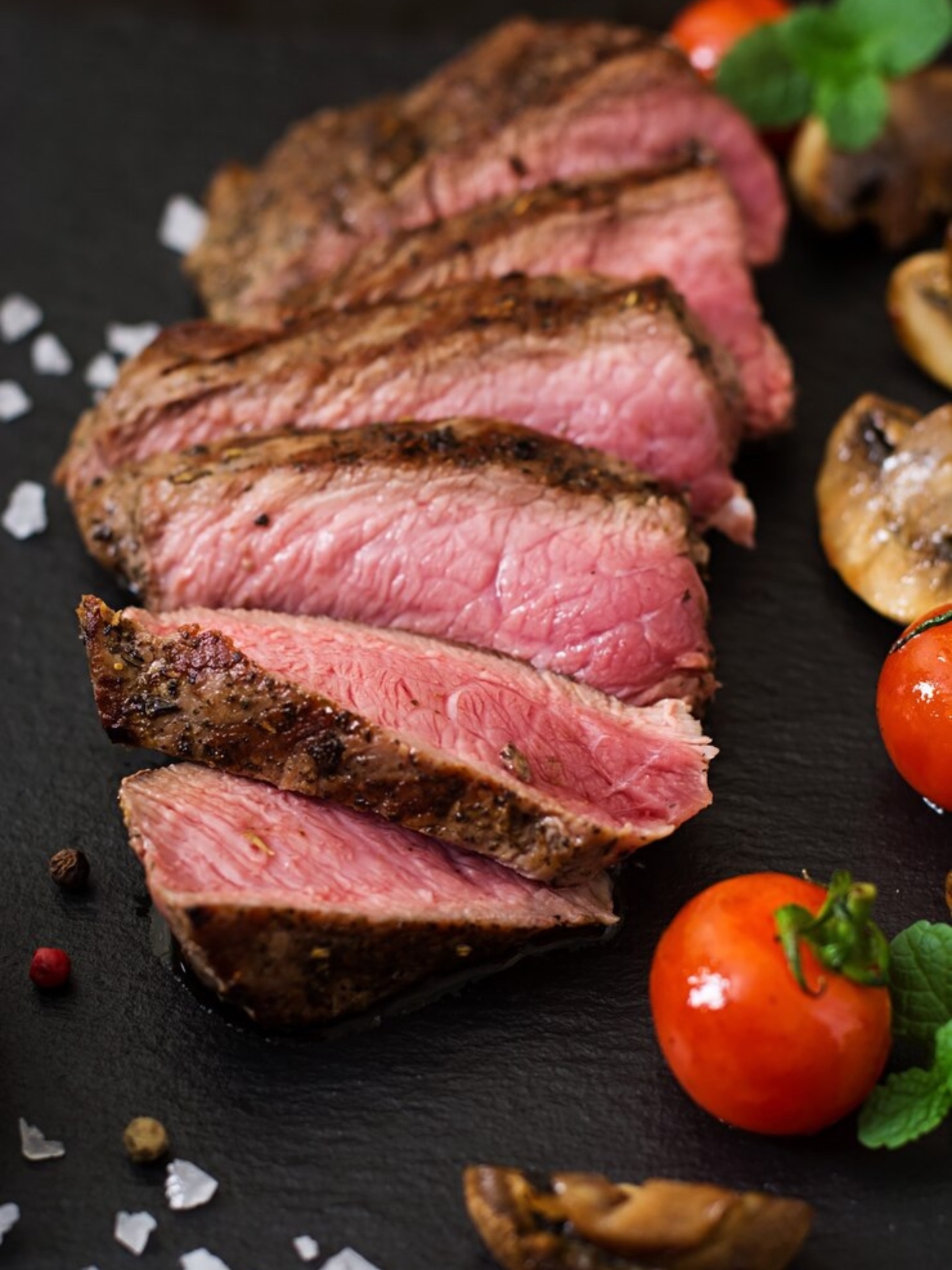 Steak Angus feliat, cu interior roz, servit cu roșii și ciuperci